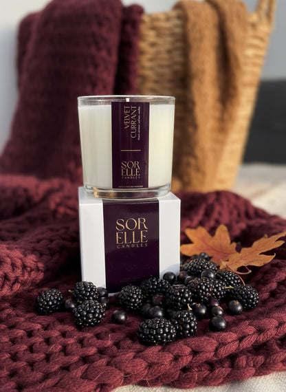 SorElle velvet currant scented coconut soy wax candle. 15oz glass candle with purple label and gold foil in fall scene